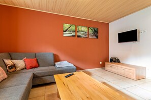 A modern living room with a grey sofa, a wooden coffee table, a TV mounted on the wall, and a small cabinet.
