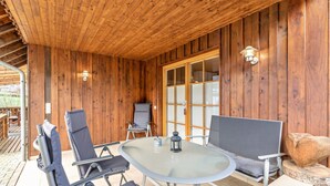 Una cabaña de madera con mesa y sillas de vidrio, un farol y un ventanal grande.