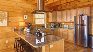 A wooden cabin kitchen with a central island, stainless steel appliances, and wooden cabinets. - Mountain Cabin, Hot Tub, Fire Pit, Views, Outdoor Bar, Stocked Kitchen (Bryson City)