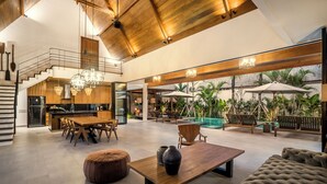 Un grand espace de vie comprenant une table à manger en bois, un canapé et un coin salon aménagé au bord de la piscine, équipé de parasols.