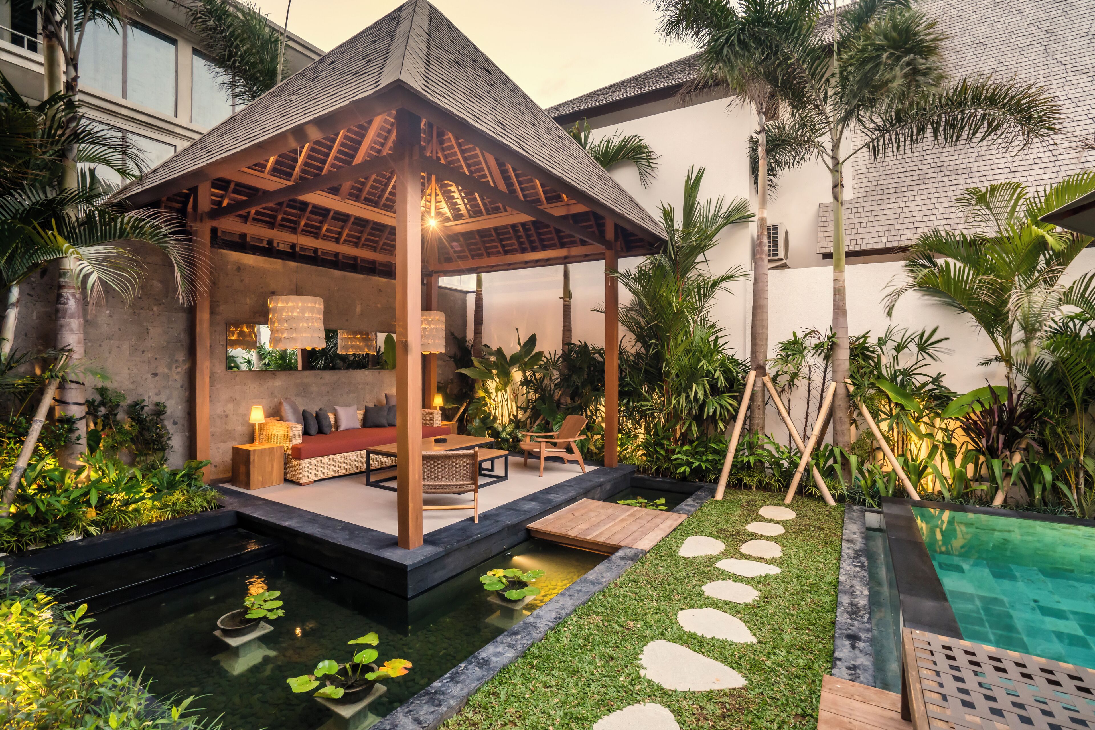 A covered outdoor seating area with a pool and garden.
