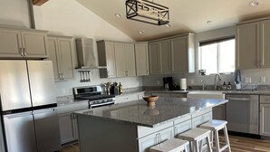 A modern kitchen with grey cabinets, stainless steel appliances, a central island with stools, and a large window providing natural light. - BIRDSEYE VIEW (Helena)