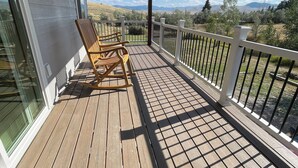 A wooden deck with a rocking chair, a white railing, and a view of a hilly landscape. - BIRDSEYE VIEW (Helena)