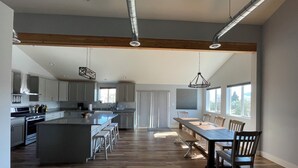 A modern kitchen with a central island, wooden flooring, and a dining area with a long table and chairs. - BIRDSEYE VIEW (Helena)