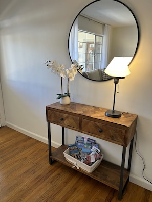Een houten console tafel met een spiegel, een vaas met witte bloemen en een lamp.