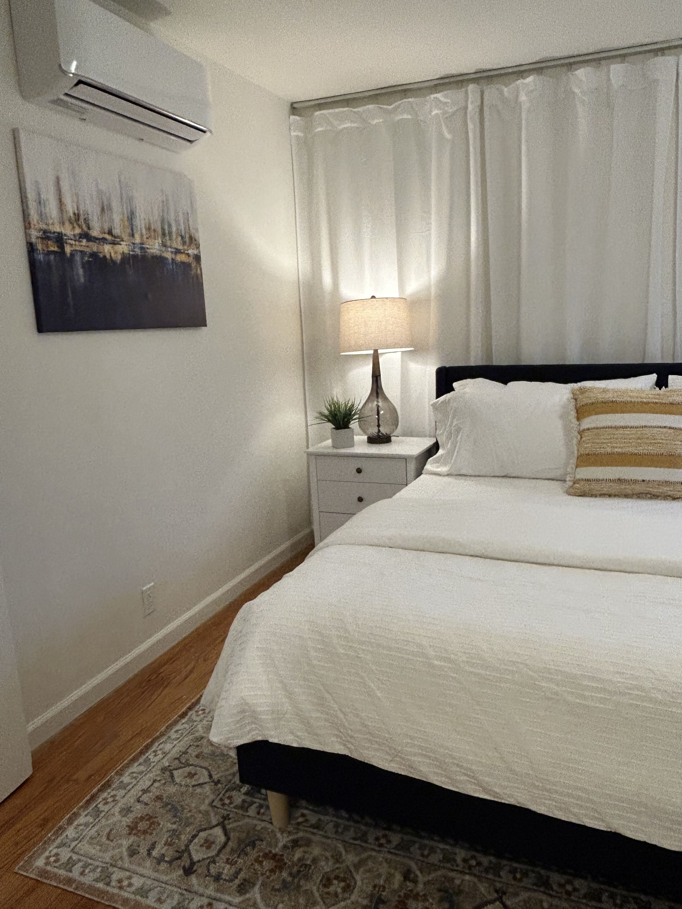 Ein ordentlich eingerichtetes Schlafzimmer mit Bett, Nachttisch, Lampe und einer kleinen Pflanze.