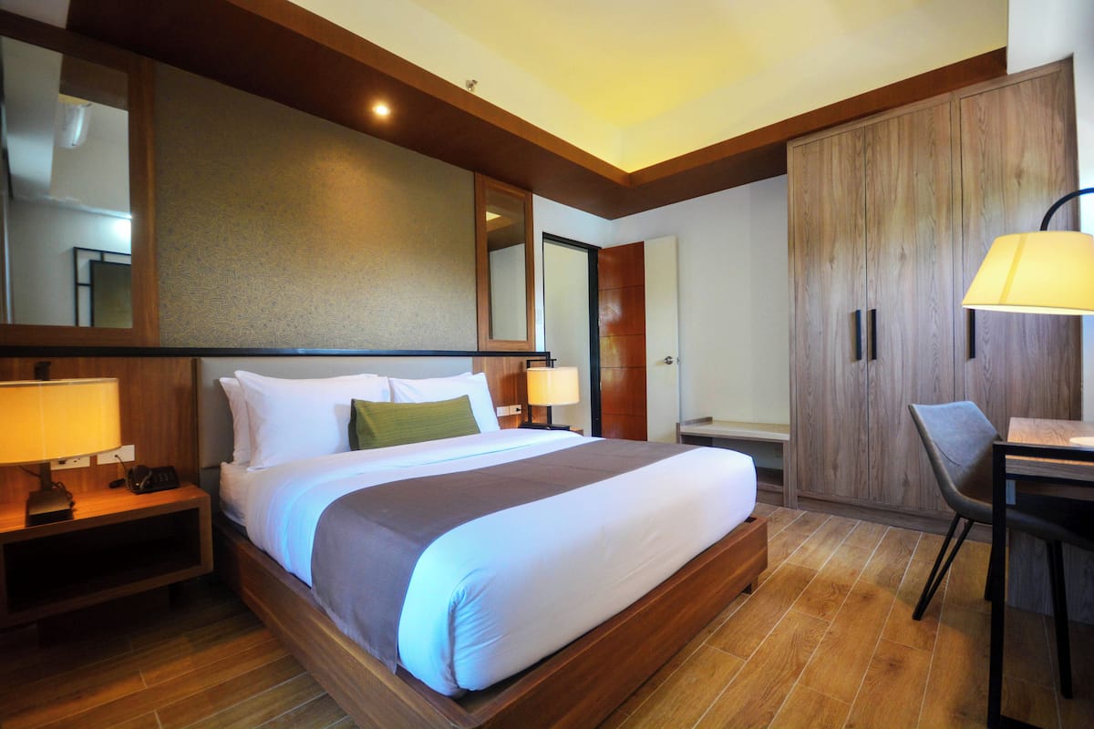 Une chambre d’hôtel avec un grand lit, des tables de chevet avec des lampes, un bureau avec une chaise et une armoire.