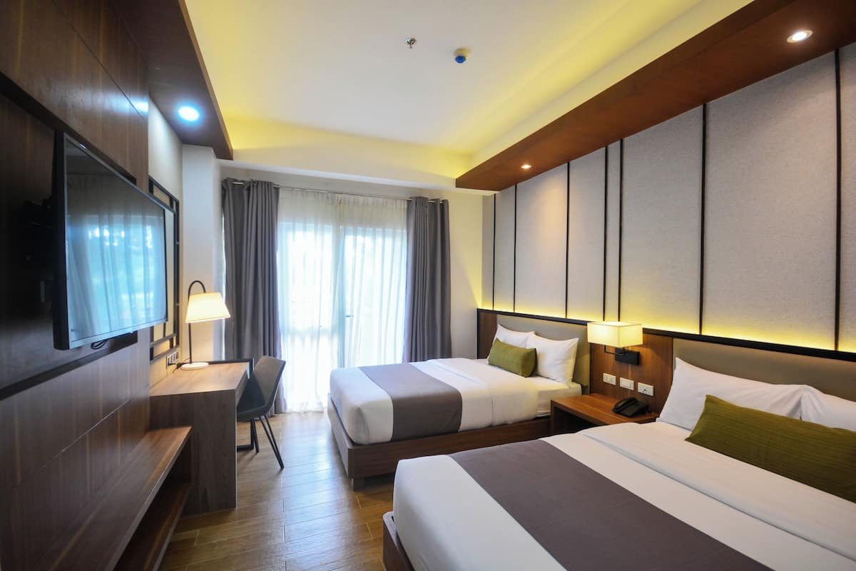 Une chambre d’hôtel avec deux lits, un bureau, une télévision et une fenêtre avec des rideaux.