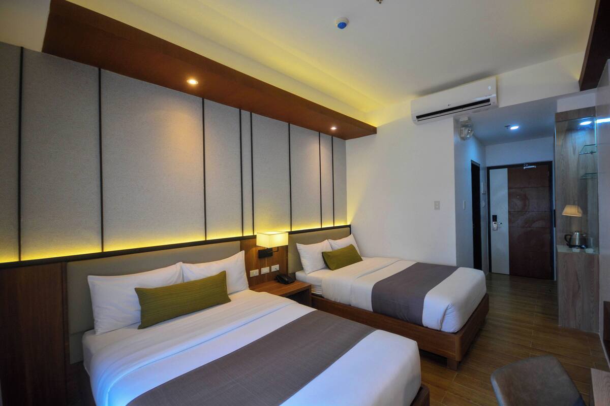 Une chambre d’hôtel avec deux lits, une tête de lit en bois, une table de chevet avec une lampe et un appareil de climatisation.