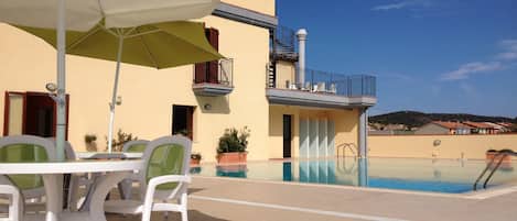 A poolside area with a table and chairs, a pool, and a building with a balcony.