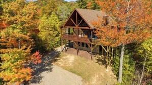 A cabin with a wooden deck, surrounded by autumn foliage. - Mountain Lodge on 57 Acres • Hiking Trails • Private Lake • Hot Tub (Murphy)