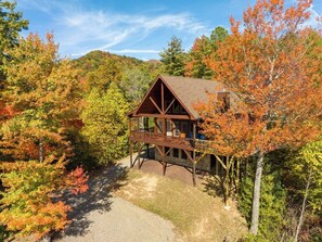 A cabin with a wooden deck, surrounded by autumn foliage.