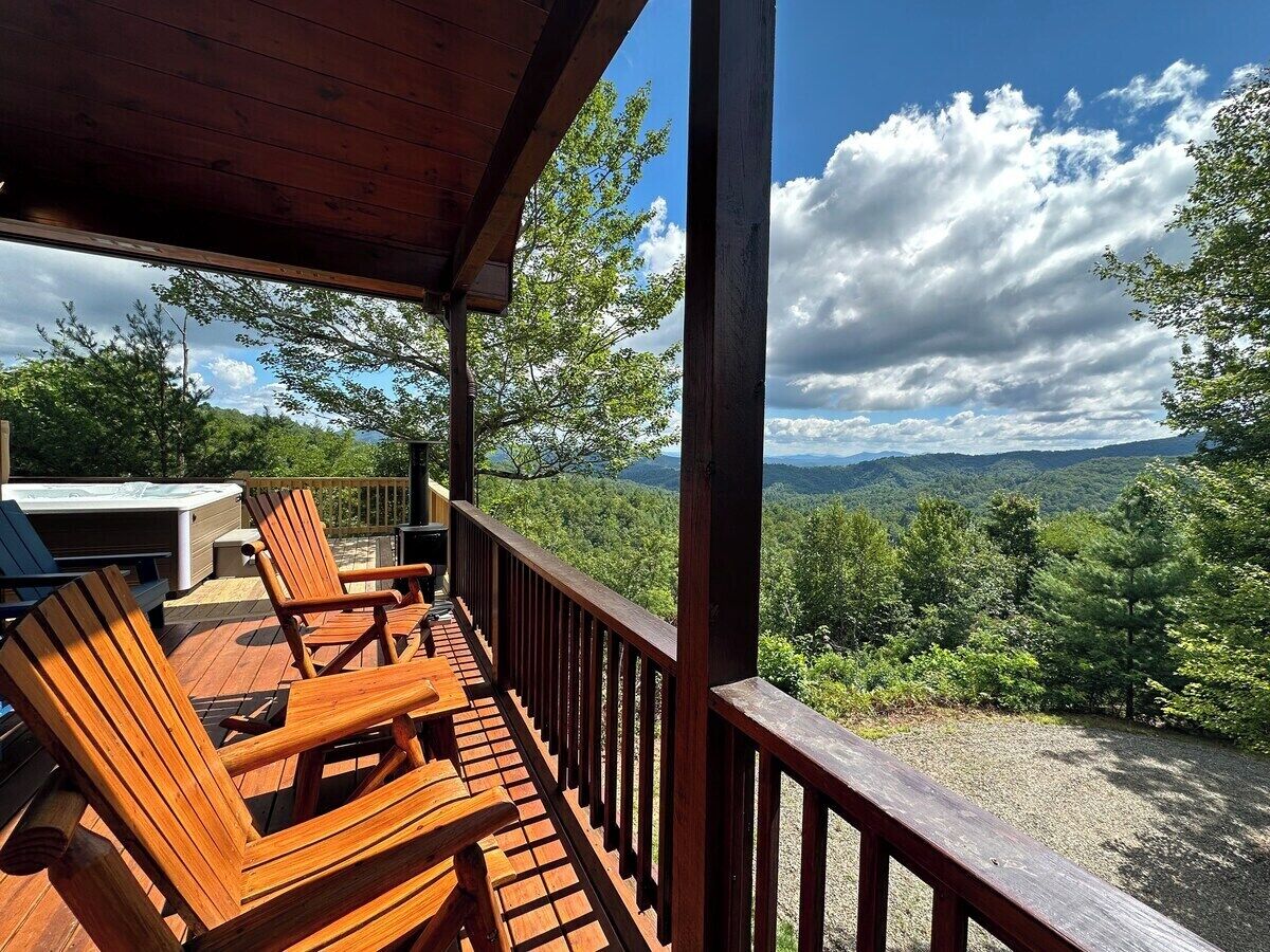 A wooden deck with chairs and a hot tub, overlooking a forested landscape.