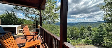 A wooden deck with chairs and a hot tub, overlooking a forested landscape.