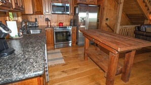 A kitchen with wooden cabinets, a granite countertop, stainless steel appliances, and a wooden dining table. - Mountain Lodge on 57 Acres • Hiking Trails • Private Lake • Hot Tub (Murphy)