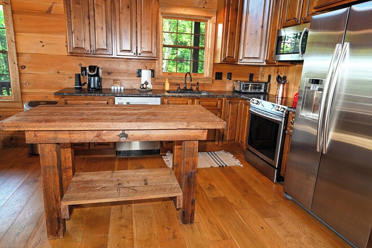 A wooden kitchen with a stainless steel refrigerator, wooden cabinets, and a wooden table.