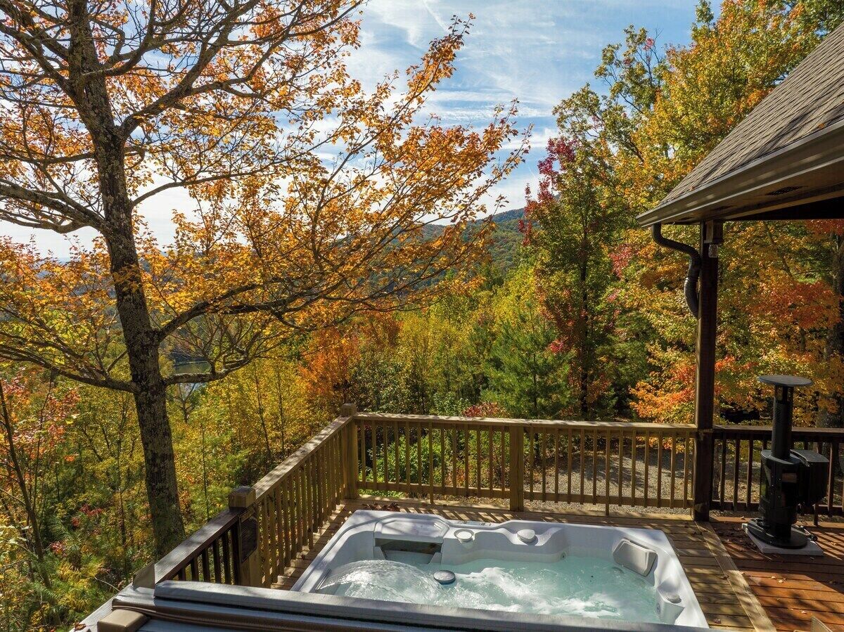 A hot tub on a wooden deck with a view of autumn foliage.
