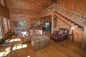A cabin interior with a wooden staircase, leather furniture, and a kitchen area.