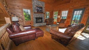 A log cabin interior with a fireplace, leather sofas, and a stone accent wall. - Mountain Lodge on 57 Acres • Hiking Trails • Private Lake • Hot Tub (Murphy)