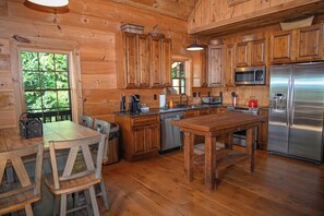 A wooden cabin kitchen with a dining table, chairs, a refrigerator, a microwave, and a sink.