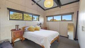 Ein Schlafzimmer mit einem Bett, Nachttischen, einer Lampe und Fenstern mit Blick auf Bäume.