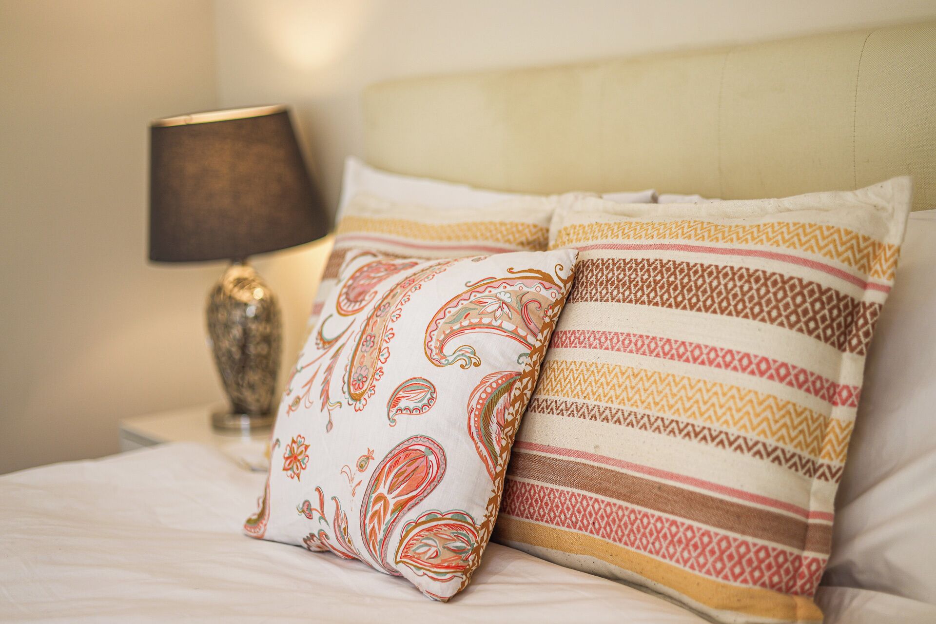 A bed with two pillows, one with paisley patterns and another with striped designs.