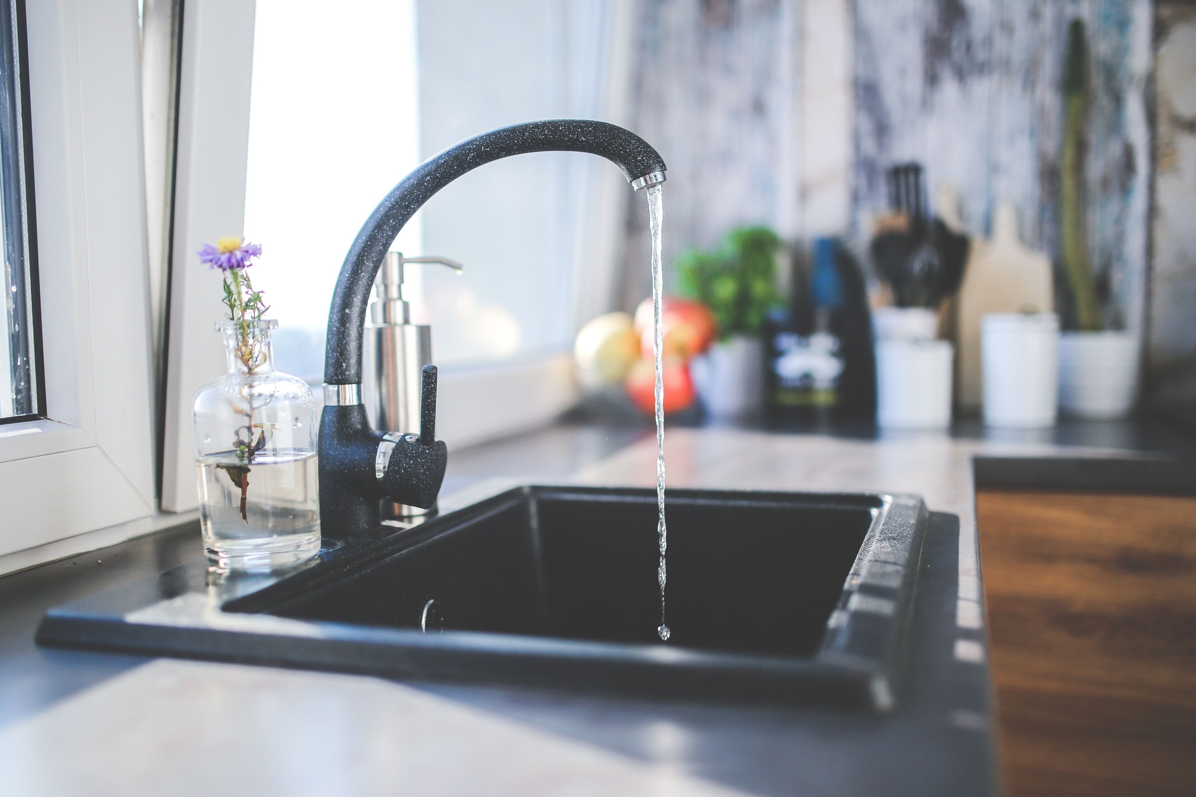 A kitchen sink with a modern faucet, a glass vase with flowers, and a window in the background.