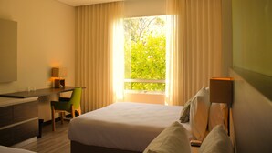 Una camera d'albergo con un letto, una scrivania, una sedia, una lampada e una finestra con tende.