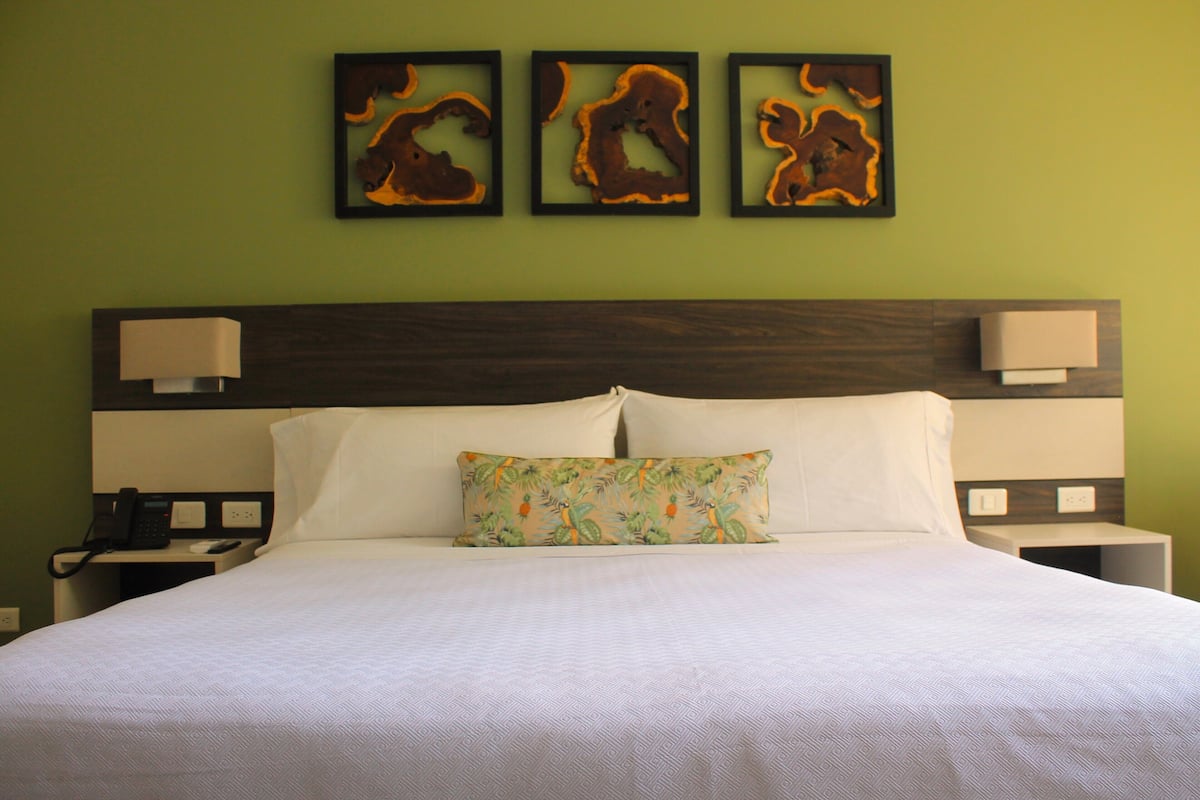 A hotel room with a large bed, two bedside tables, a nightstand, and a wall-mounted telephone.