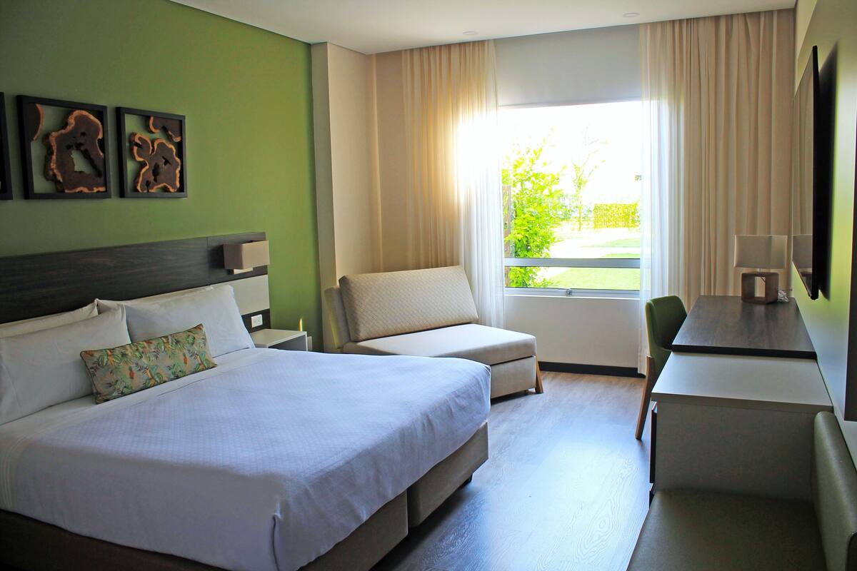 A hotel room with a large bed, two armchairs, a desk, and a TV.