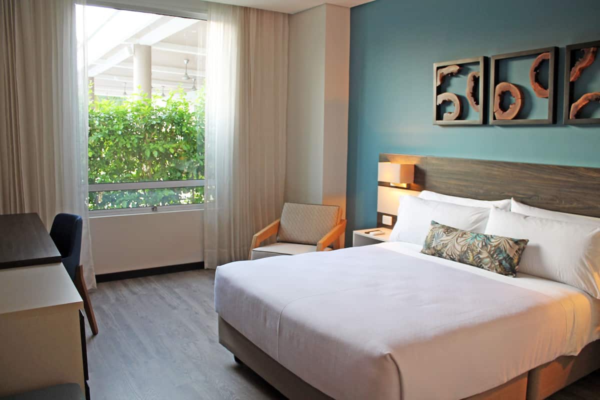 A hotel room with a large bed, a desk, a chair, and a window with curtains.