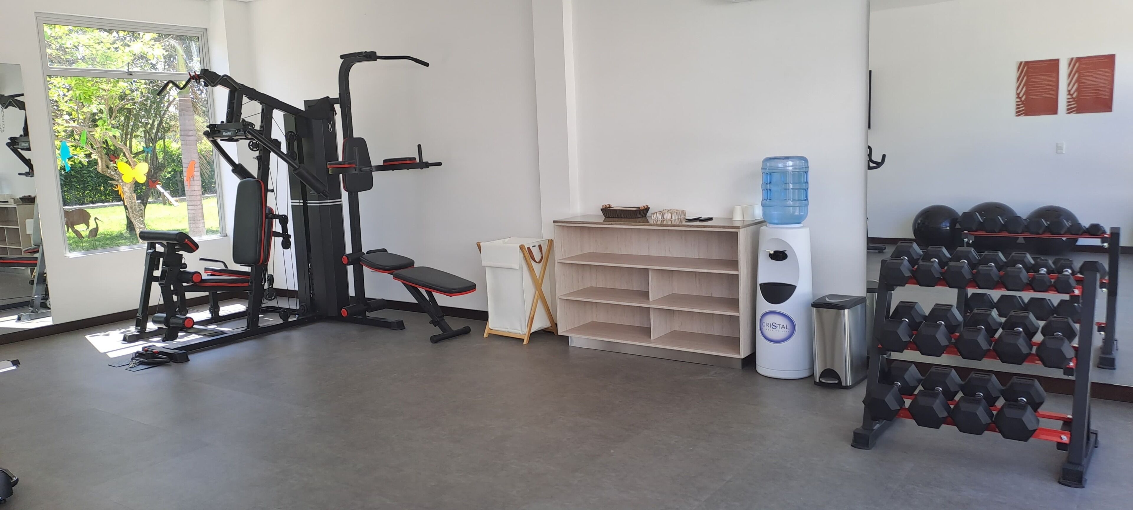 Un gimnasio con equipo de ejercicio, un dispensador de agua y un estante con mancuernas.