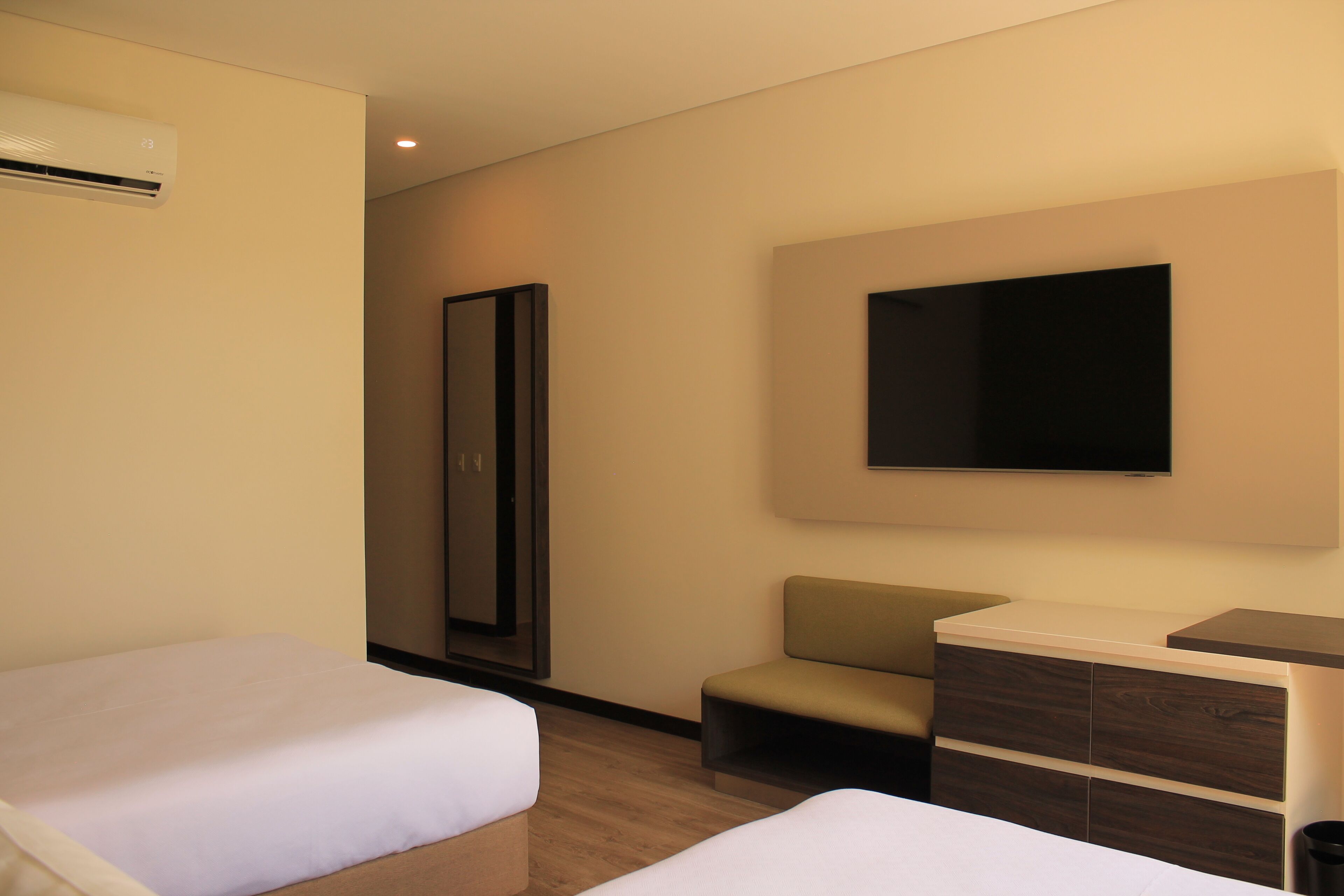 A hotel room with two beds, a flat-screen TV mounted on the wall, a small seating area, and a wooden dresser.