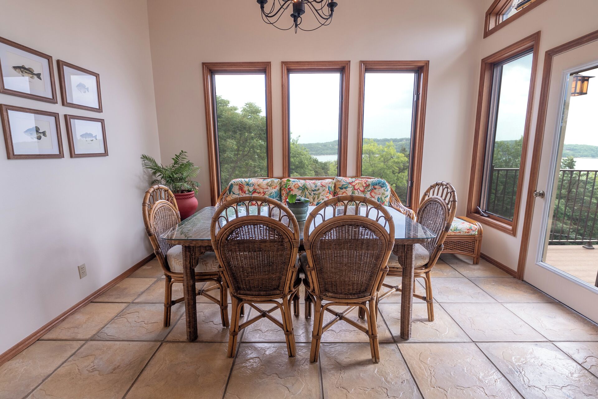 A dining area with a glass table and wicker chairs, large windows with a view, and framed pictures on the wall.