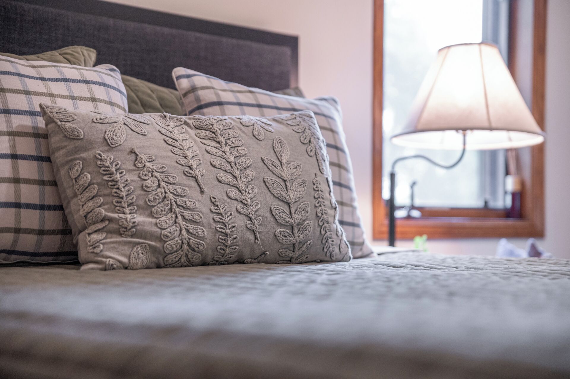 A bed with a plaid blanket and decorative pillows, a bedside lamp, and a window with a view.