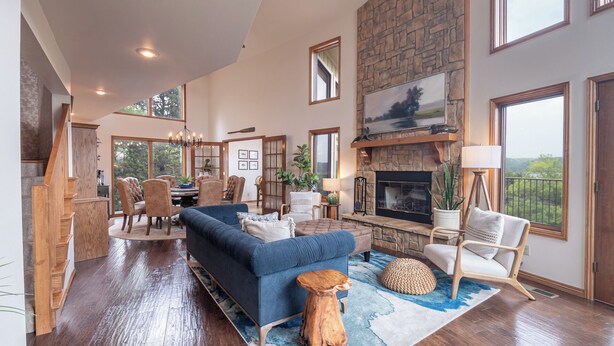 A spacious living room with a stone fireplace, a dining area with a large window, and a cozy seating area with a blue sofa and wooden coffee table. - Lost Bridge Lodge on BEAVER LAKE! Across from POOL (Garfield)