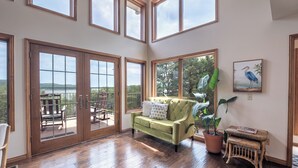 A spacious room with a green sofa, wooden flooring, and large windows offering a view of the outdoors. - Lost Bridge Lodge on BEAVER LAKE! Across from POOL (Garfield)