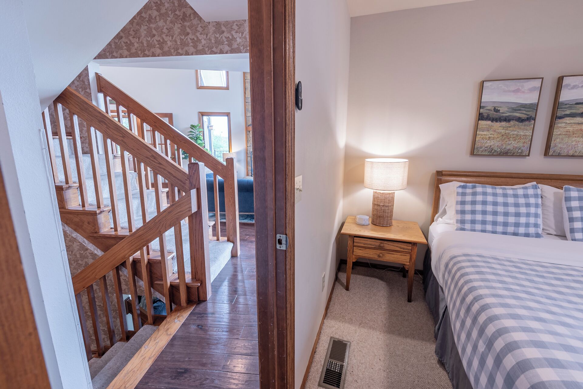 A bedroom with a bed, a nightstand, a lamp, and a window with a view of the countryside.