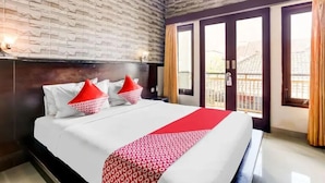 A hotel room with a large bed, a brick-patterned wall, and a view of the outside through a sliding door. - Antara Sunset Road (Denpasar)