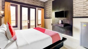 A hotel room with a bed, a flat-screen TV mounted on the wall, a minibar, and a balcony with curtains. - Antara Sunset Road (Denpasar)