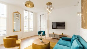 A modern living room with a round coffee table, a teal sofa, and a mustard-colored armchair. - Merveil - Family Suite - Louvre - Sainte Anne (Paris)