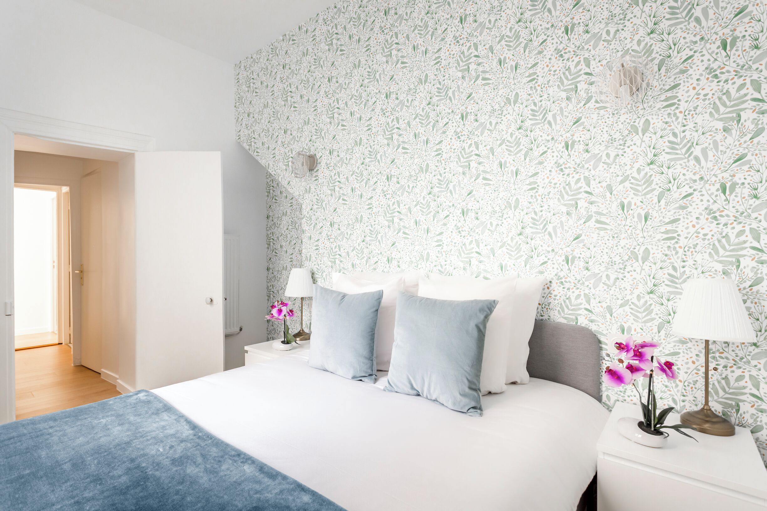 A bedroom with a large bed, two bedside tables, and a floral wallpaper.