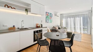 Een moderne keuken met witte kasten, een eettafel met stoelen, en een zithoek met een bank en gordijnen.
