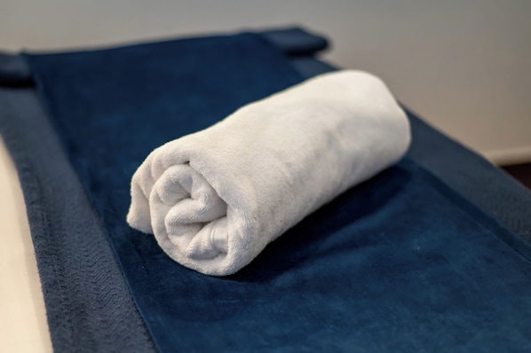 Une serviette blanche, soigneusement pliée, est posée sur une serviette bleu foncé, sur un lit.