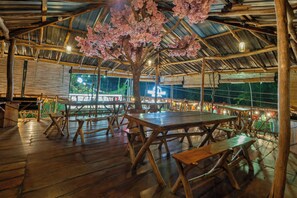 Une terrasse extérieure en bois, dotée de tables et de bancs, et entourée d’une structure de toit en métal.