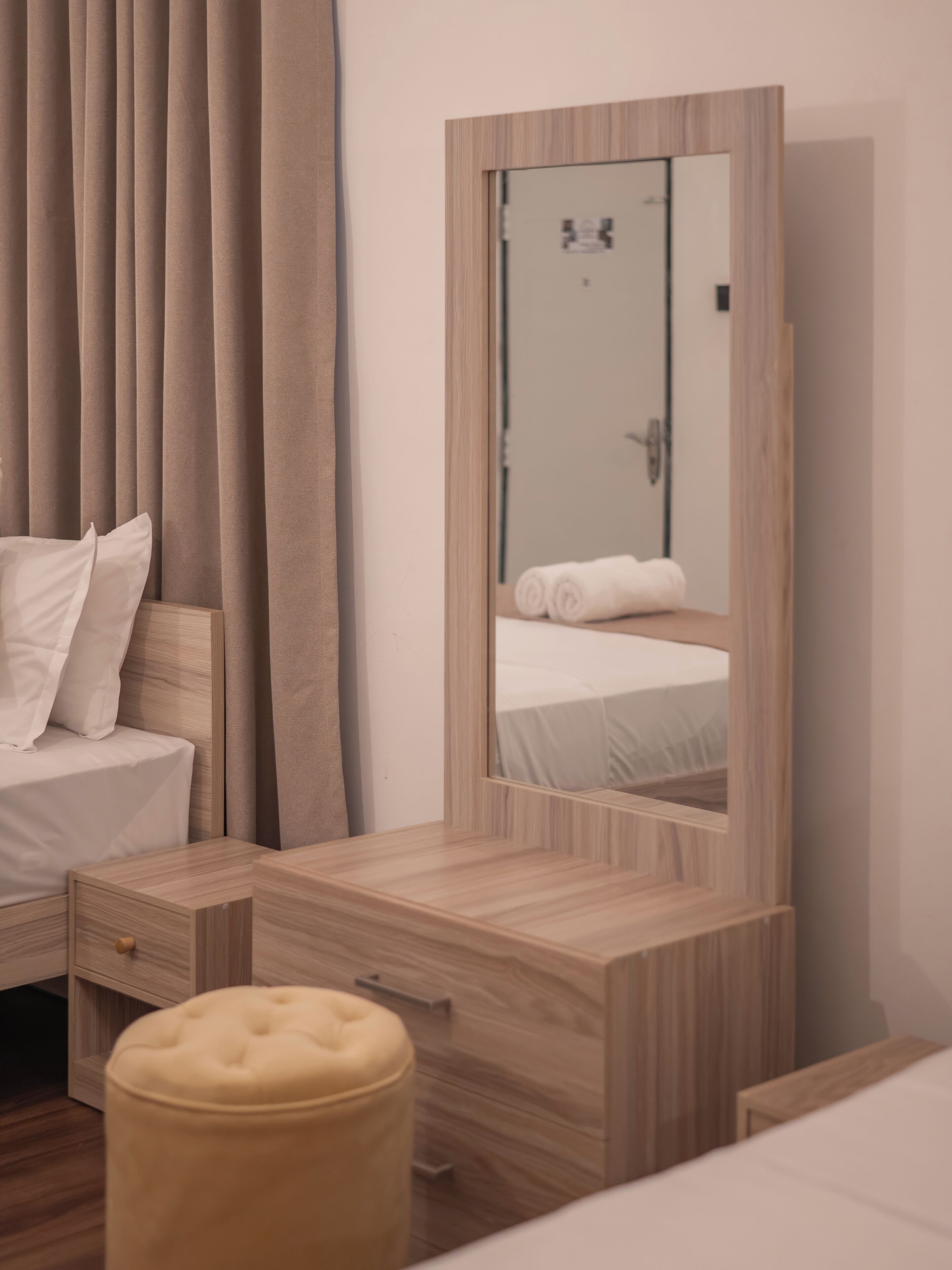 Ein Schlafzimmer mit einem Bett, einem Nachttisch aus Holz, einem Spiegel und einem Fenster mit Vorhängen.