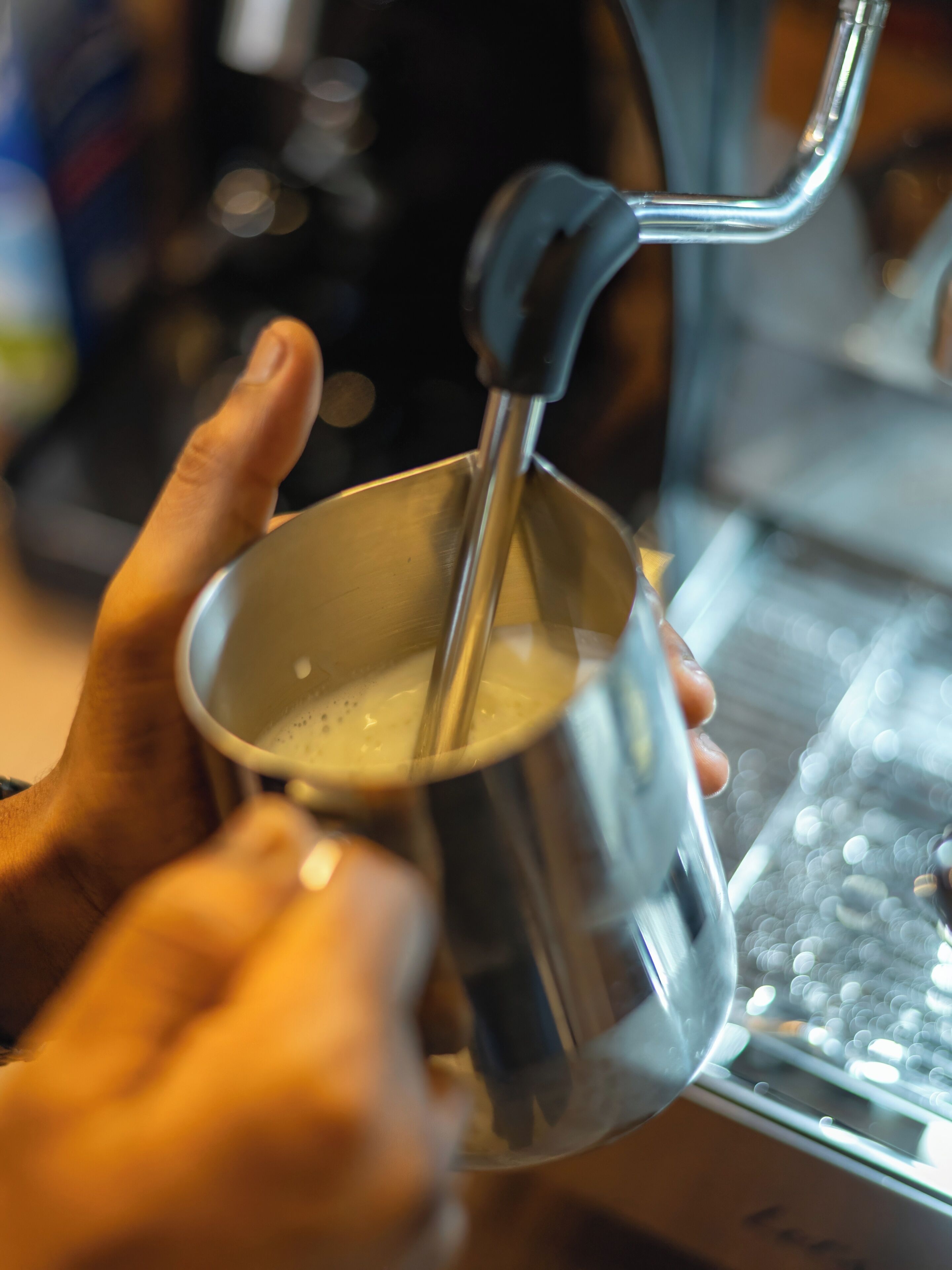 Una persona sosteniendo una taza de metal con una cuchara, probablemente en una cocina o cafetería.