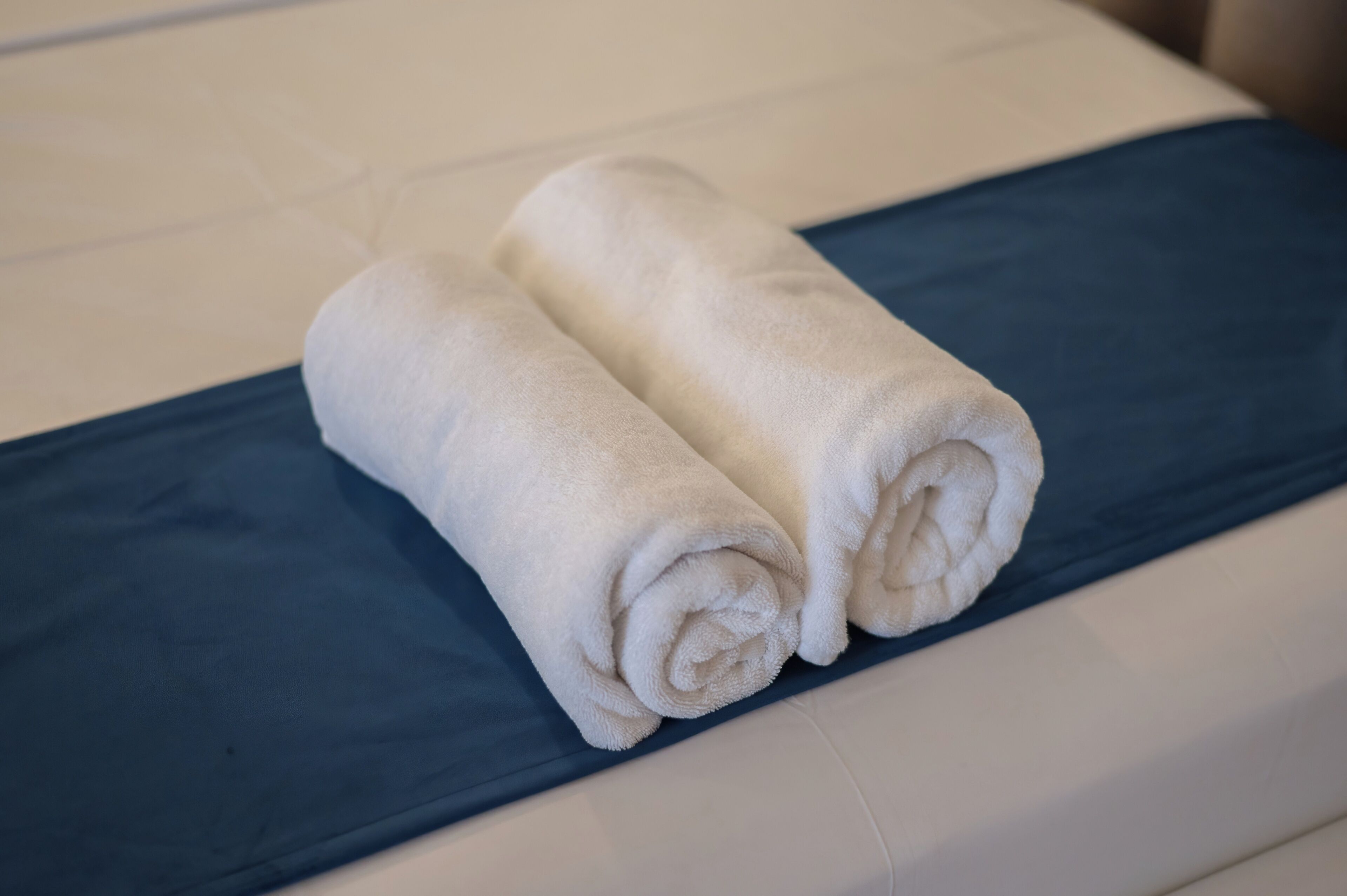 Ein ordentlich bezogenes Bett mit einer blauen Bettdecke und zwei aufgerollten weißen Handtüchern darauf.