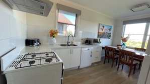 A modern kitchen with a gas stove, a dishwasher, a microwave, and a sink. There is a dining area with wooden chairs and a table. - Morwell Pet friendly 3BM House (Morwell)