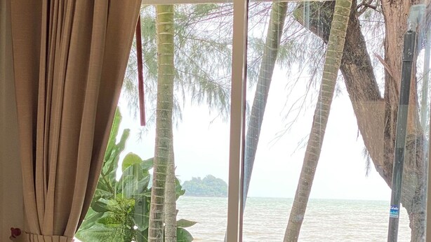 Una habitación con vista a la playa, una mesa redonda de madera y una cortina.